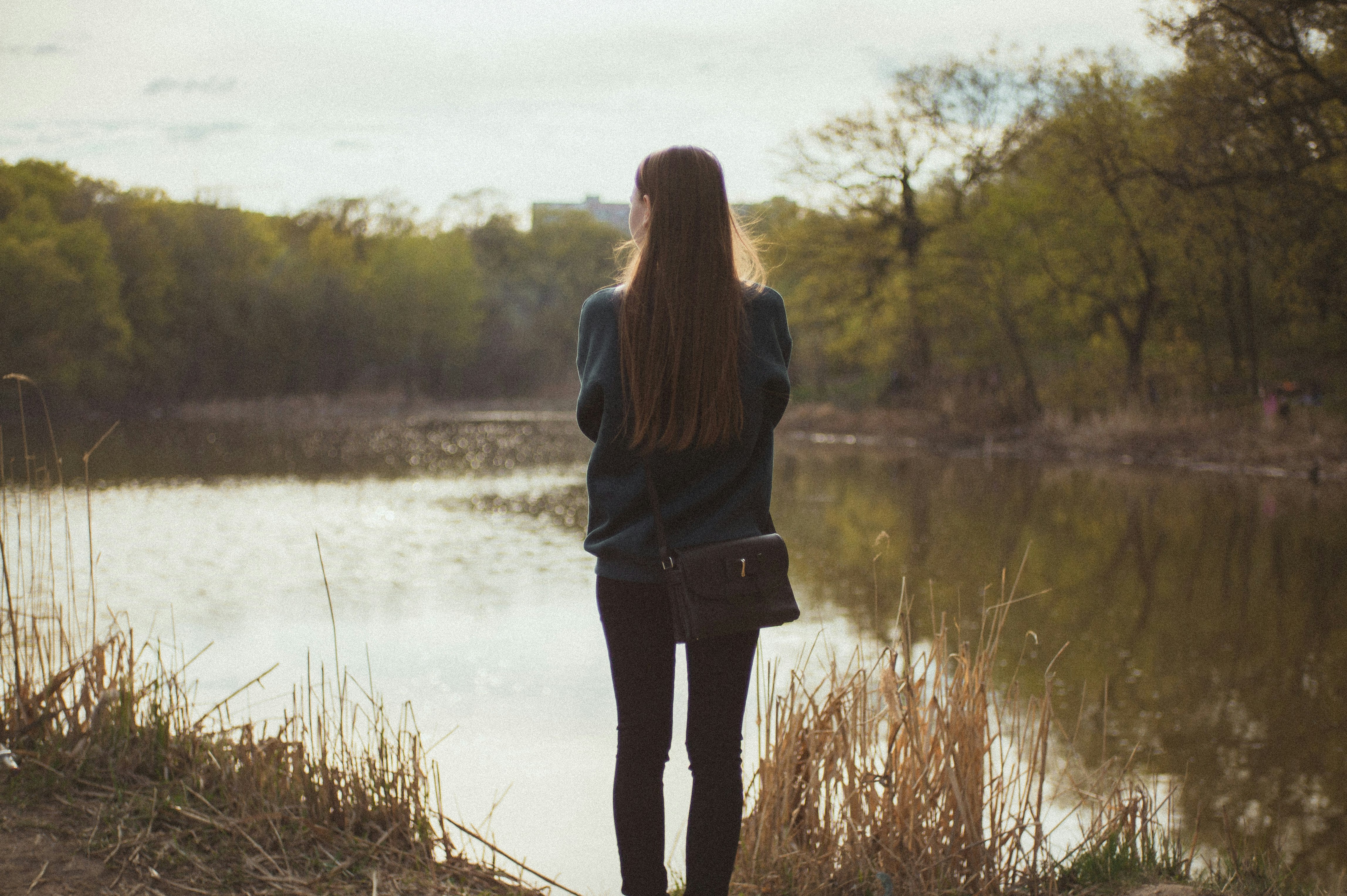 woman in black jacket standing on brown grass field near lake during daytime